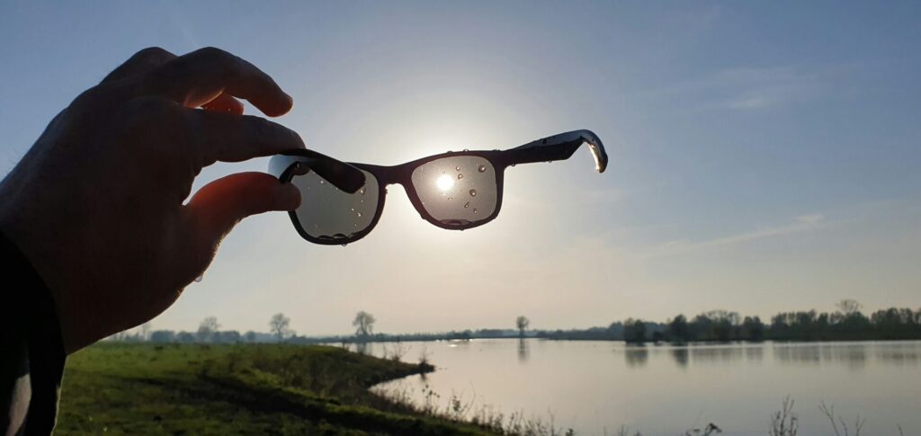 a person holding a pair of sunglasses in front of a lake