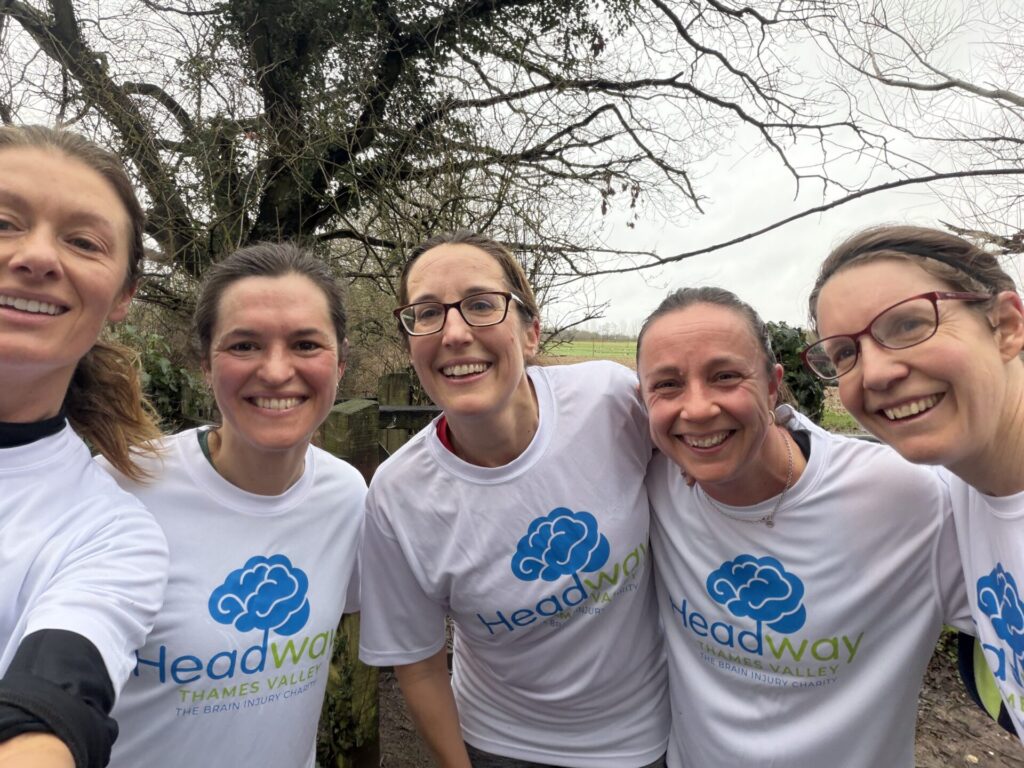 A group of people wearing matching white “Headway Thames Valley – The Brain Injury Charity” T‑shirts pose together outdoors on a cloudy day