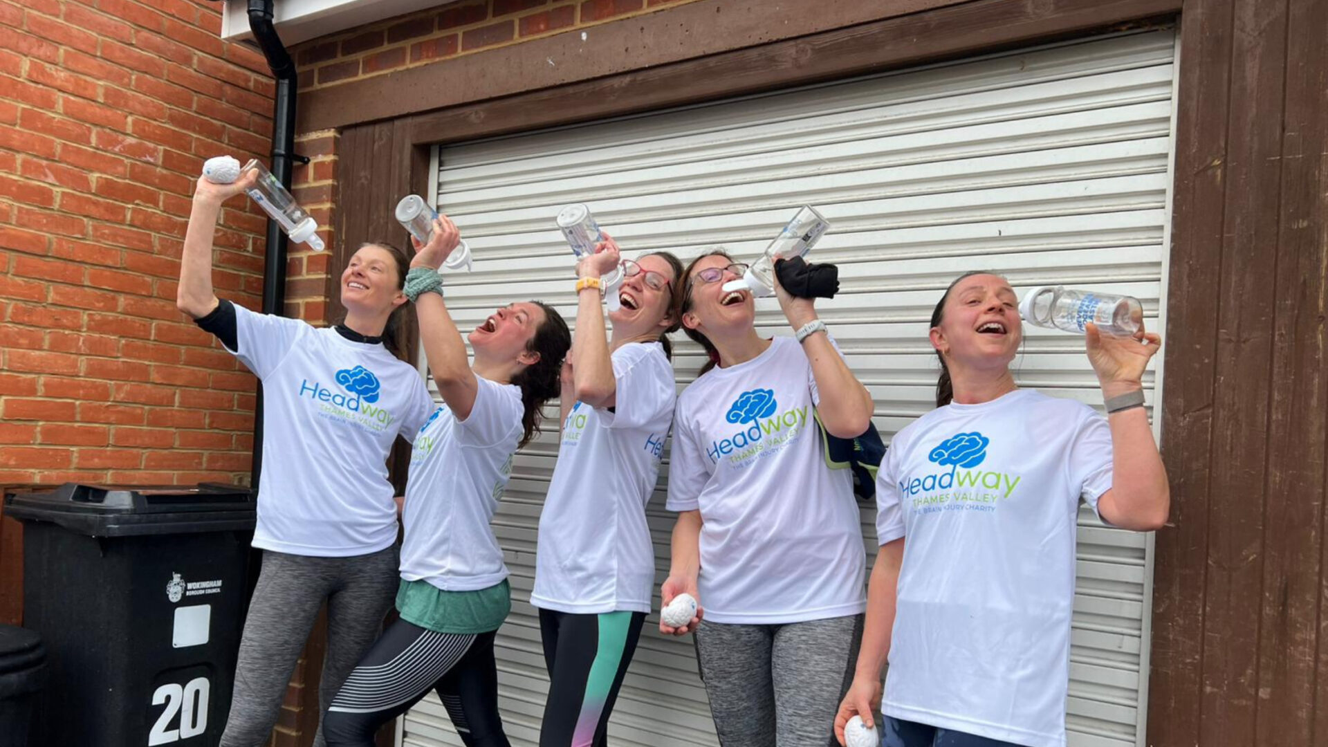 Five people in Headway Thames Valley T‑shirts pose with water bottles after a run, standing in front of a white garage door.
