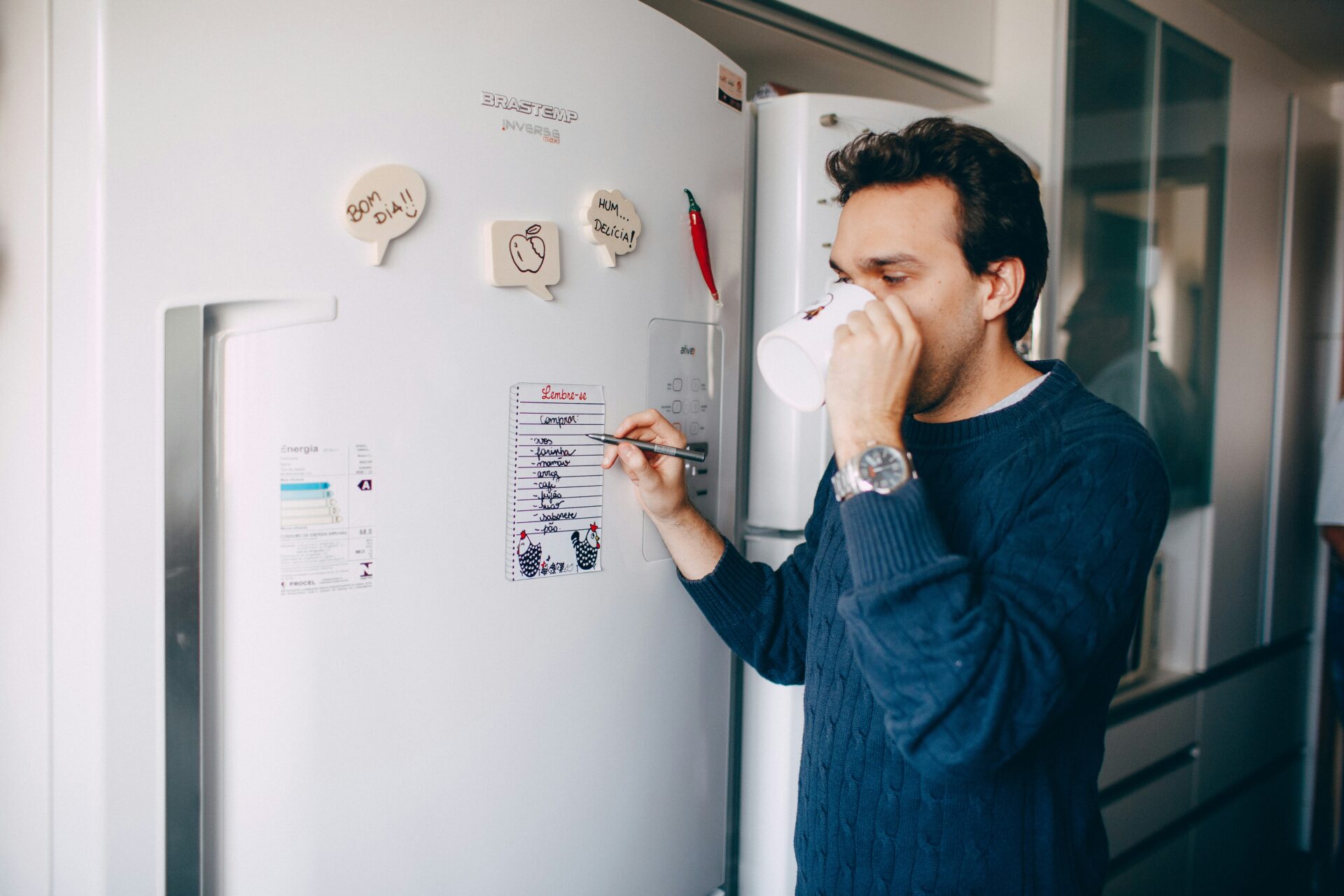 Person standing by a kitchen fridge marking a checklist. Scene reflects coping strategies for brain trauma memory loss through visual reminders and task tracking.