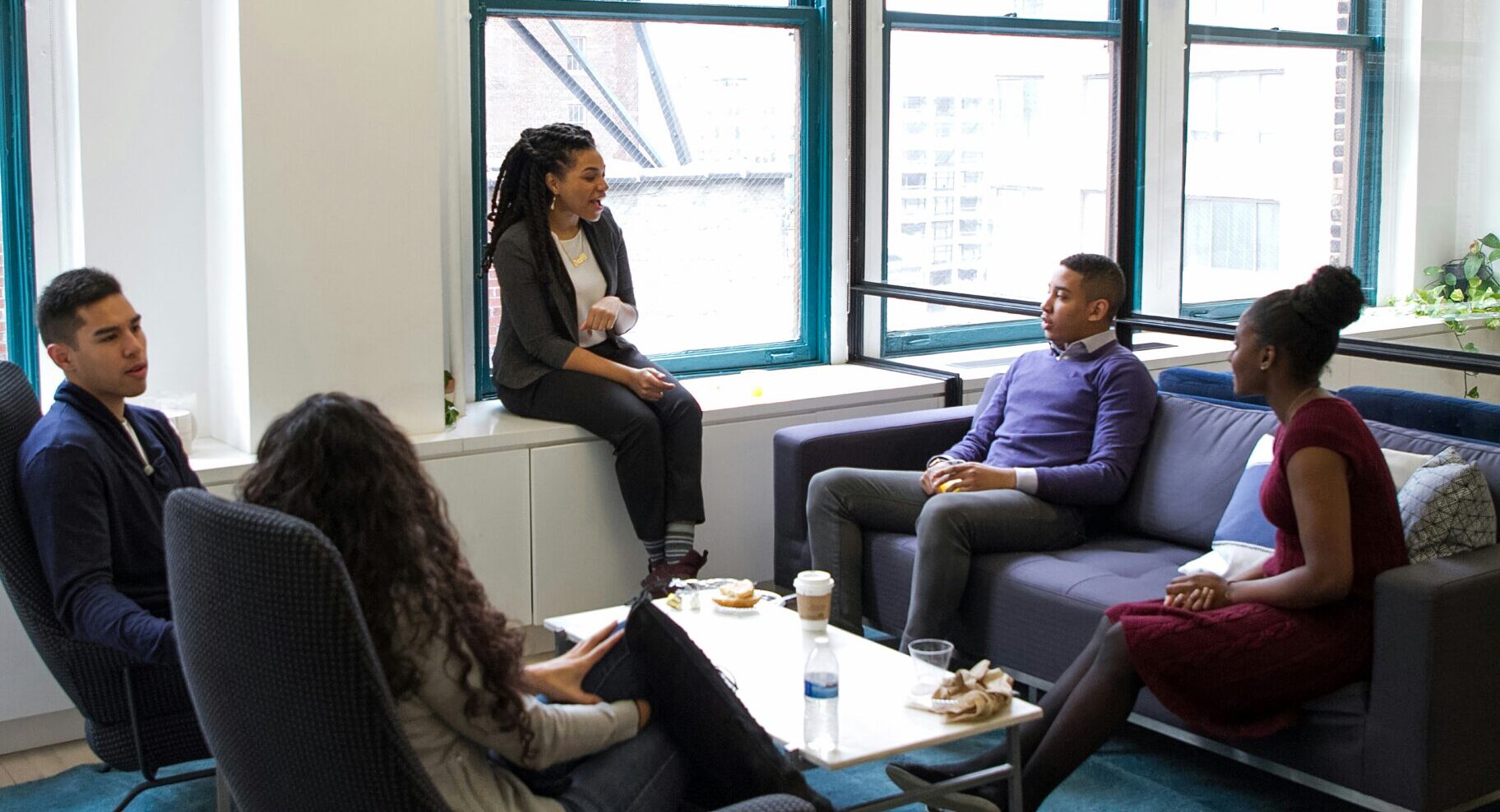 Five people seated and gathered in a bright modern office lounge, introducing themselves in a small group