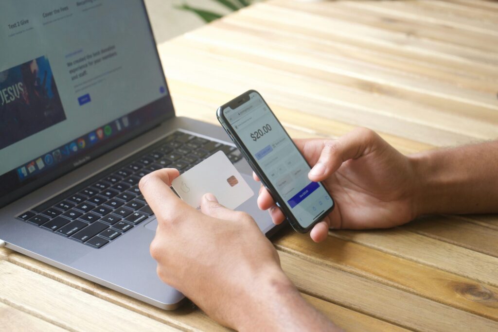 Person using a smartphone banking app and credit card beside a laptop, representing concept image for financial help after brain injury