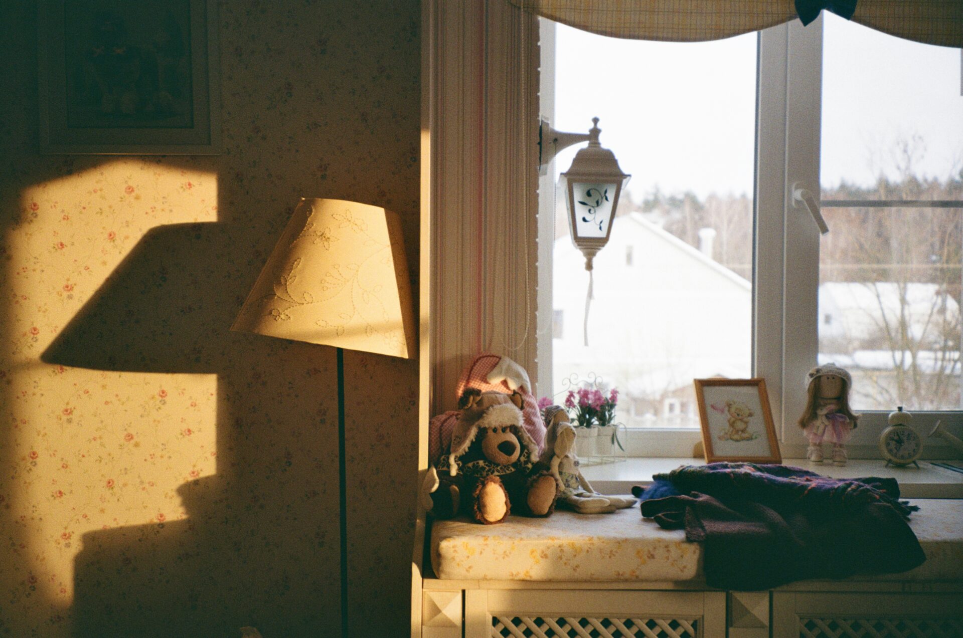 vintage bedroom corner with a window seat, teddy bear, figurines, and winter view outside, evoking brain trauma memory loss through nostalgic, shadow-filled composition.